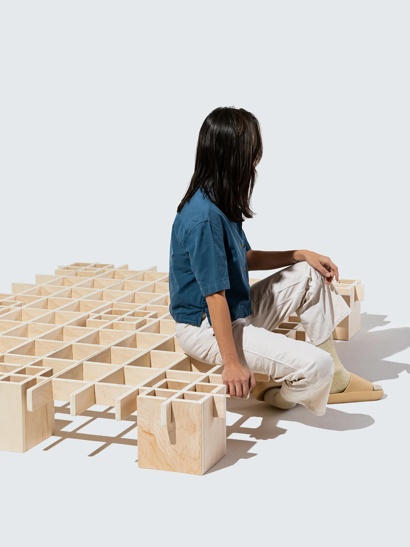 A person in a blue shirt sitting on the Tic Tac Toe bed frame by Quagga Designs.
